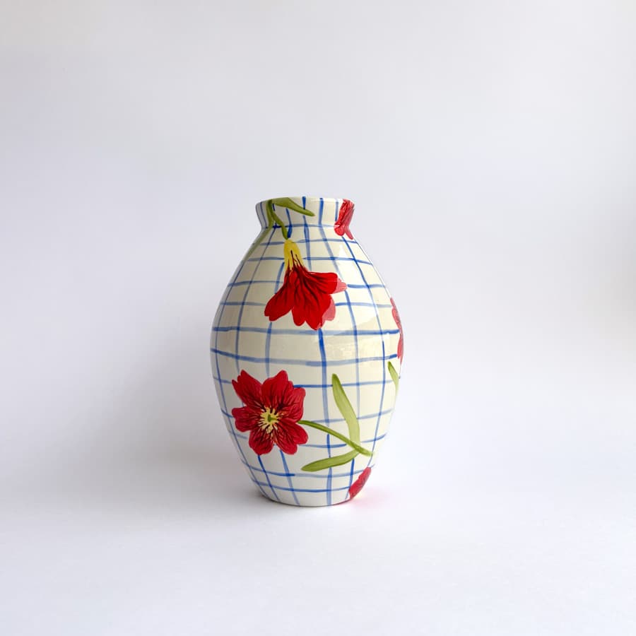 Florero cerámica panza de burro con diseño de cuadros azules y flores rojas, en vista lateral derecha sobre fondo claro