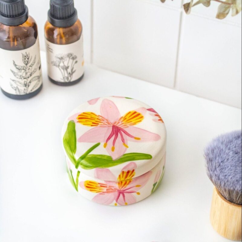 Joyero astromelia rosada con diseño de flora nativa de Chile, vista superior en un escenario de tocador con botellas y brocha