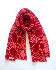 Bufanda tejida inspirada en flora nativa chilena, colores rojo y coral, confeccionada con hilado de alta calidad.