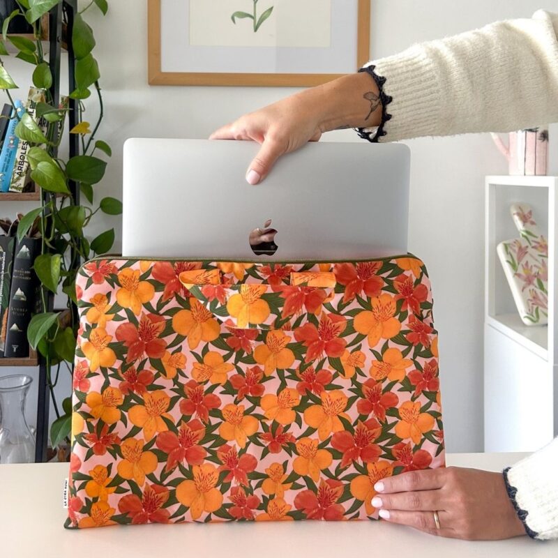 Persona insertando laptop en funda notebook astromelias en oficina, vista frontal con decoración de flora nativa de Chile
